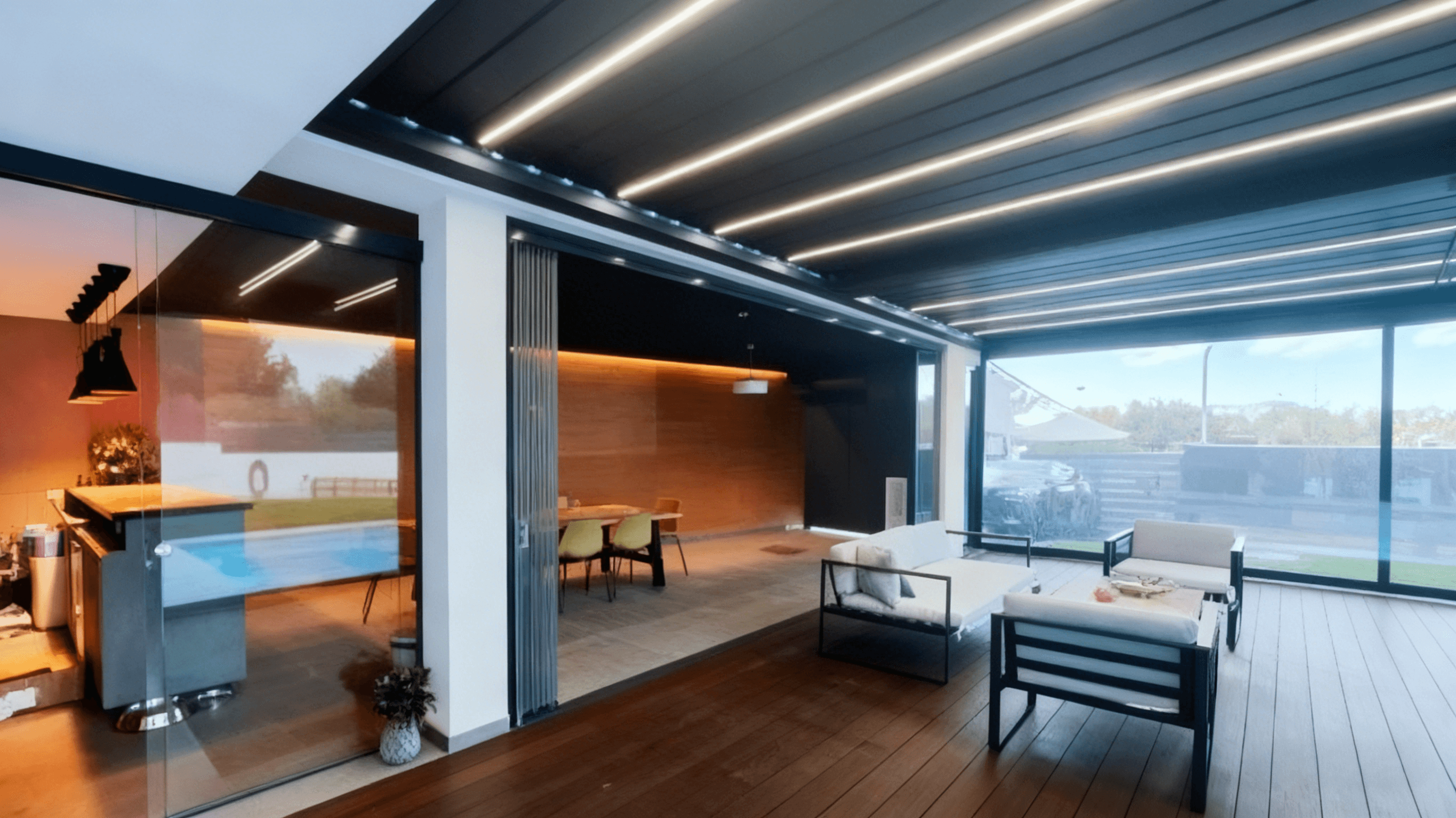 Outdoor kitchen and lounge area under an aluminum pergola with glass enclosure